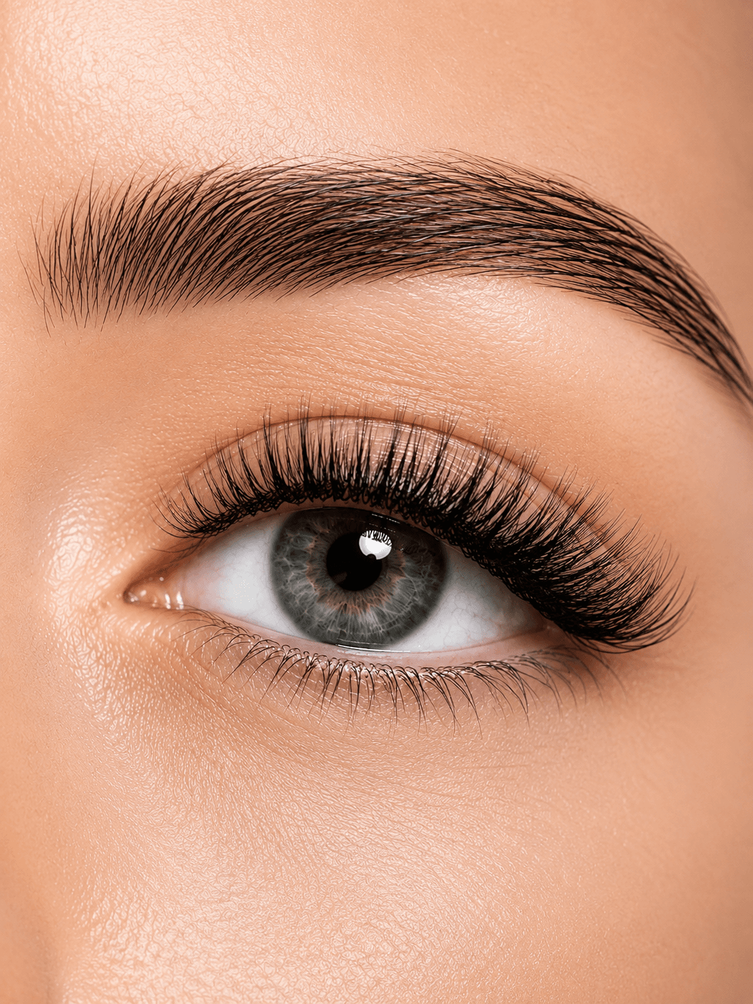Close-up of a green eye with long, voluminous black eyelashes and a groomed dark eyebrow.