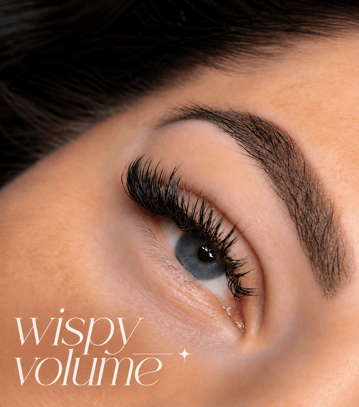 Close-up of blue eye with long, thick wispy volume eyelash extensions and defined eyebrow.