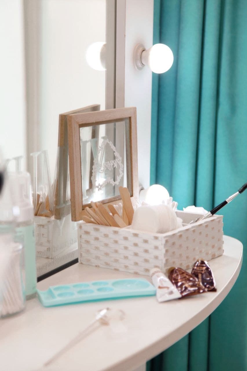 White vanity table featuring beauty tools, a lighted mirror, and vibrant teal curtains.